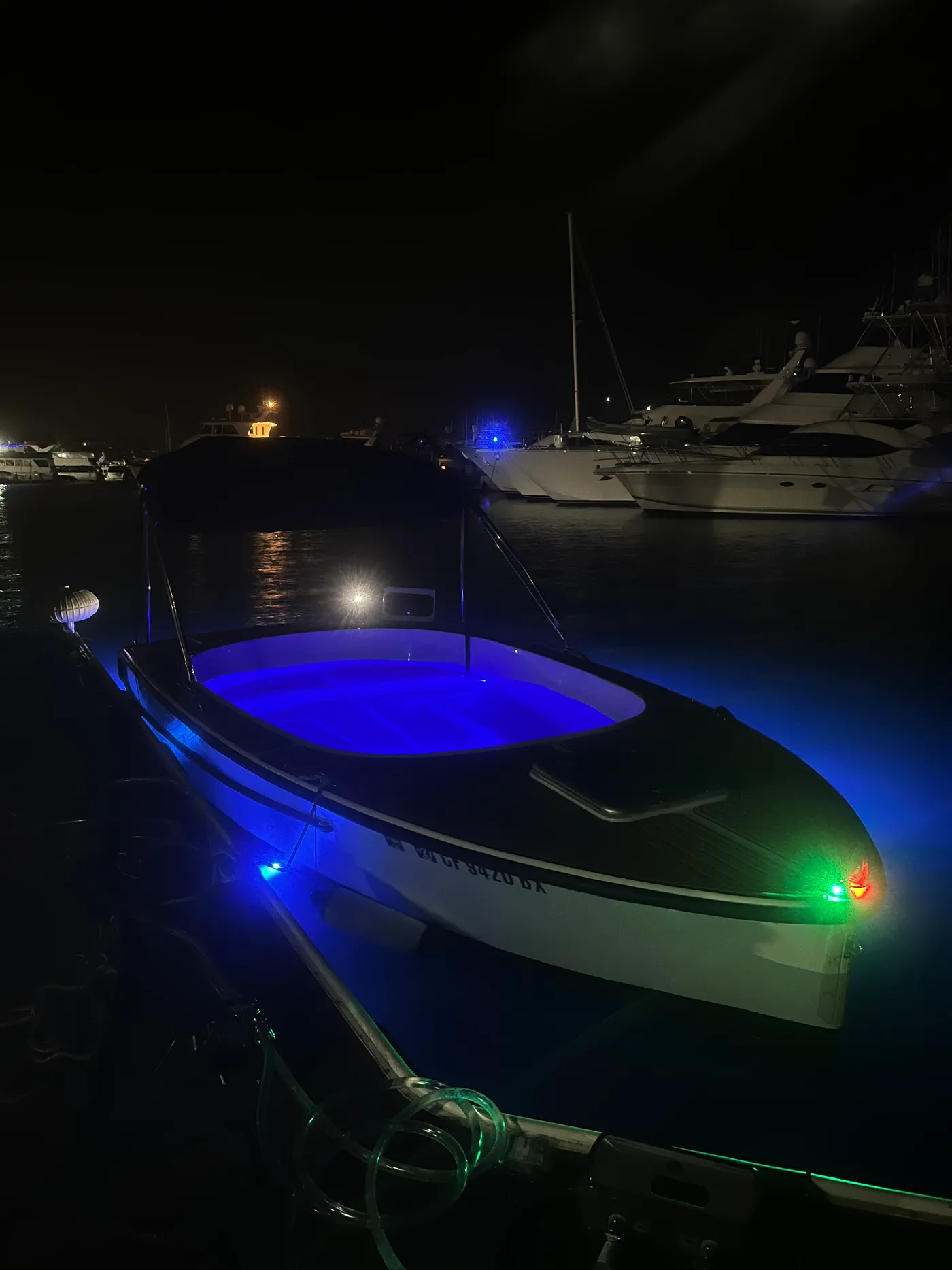 The hot tub boat tied up at the Newport Beach dock after dark, CA registration numbers on the hull, navigation lights and underwater LEDs lit