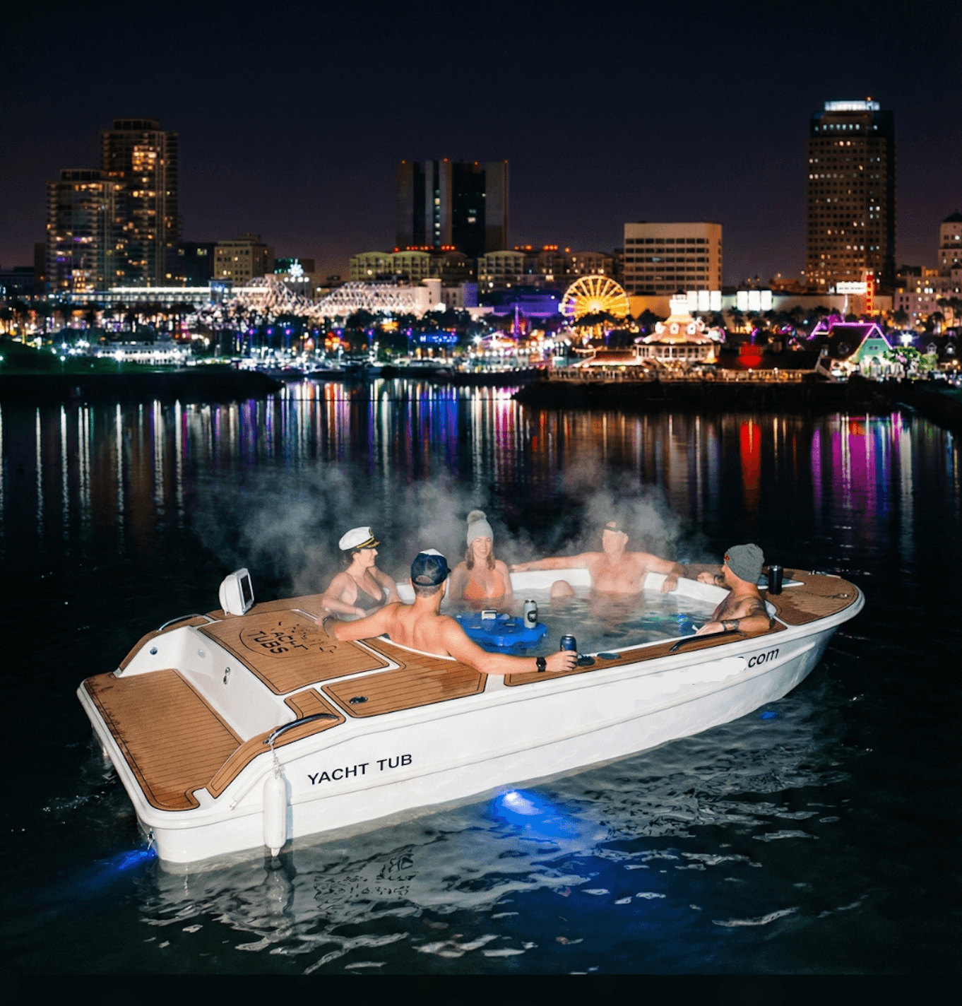 The hot tub boat at night, steam rising off the water against a lit skyline